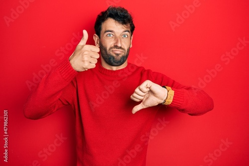 Handsome man with beard wearing casual red sweater doing thumbs up and down, disagreement and agreement expression. crazy conflict © Krakenimages.com
