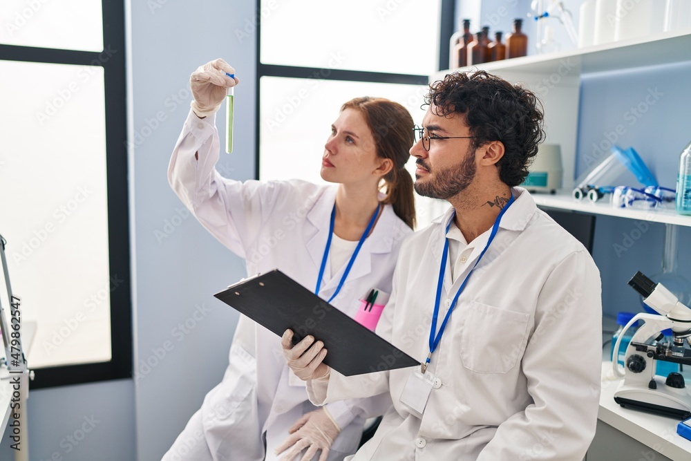 Man and woman scientist partners looking test tube holding clipboard at laboratory Man and woman scientist partners looking test tube holding clipboard at laboratory