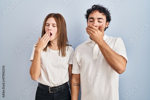 Young couple wearing casual clothes standing together bored yawning tired covering mouth with hand. restless and sleepiness.