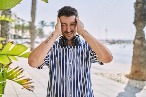 Fotografie Young handsome man listening to music using headphones outdoors suffering from headache desperate and stressed because pain and migraine