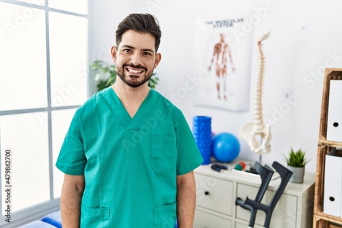 Young man with beard working at pain recovery clinic with a happy and cool smile on face. lucky person.