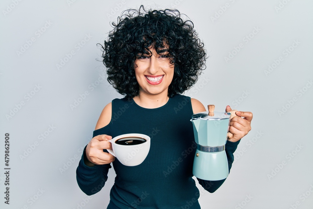 Young middle east woman holding italian coffee maker winking looking at the camera with sexy expression, cheerful and happy face. Young middle east woman holding italian coffee maker winking looking at the camera with sexy expression, cheerful and happy face.