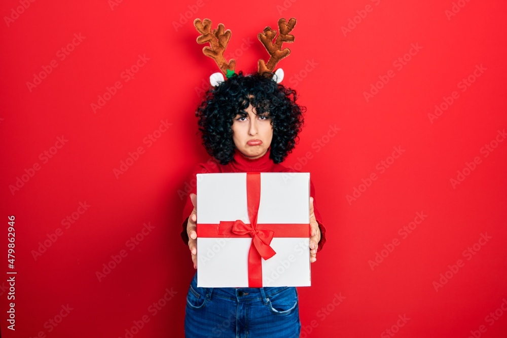 Young middle east woman wearing deer christmas hat holding gift depressed and worry for distress, crying angry and afraid. sad expression. Young middle east woman wearing deer christmas hat holding gift depressed and worry for distress, crying angry and afraid. sad expression.