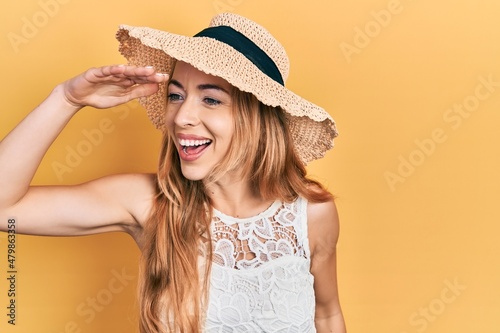Young caucasian woman wearing summer hat very happy and smiling looking far away with hand over head. searching concept.