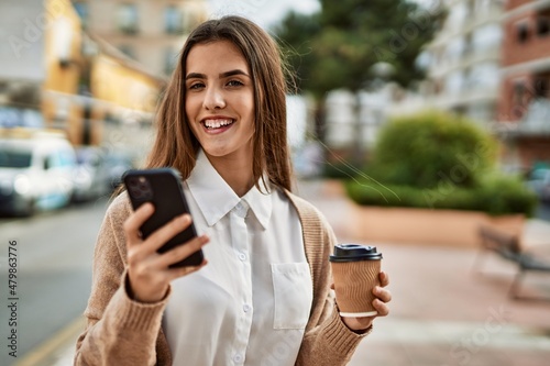 Young hispanic businesswoman using smartphone drinking coffee at the city.