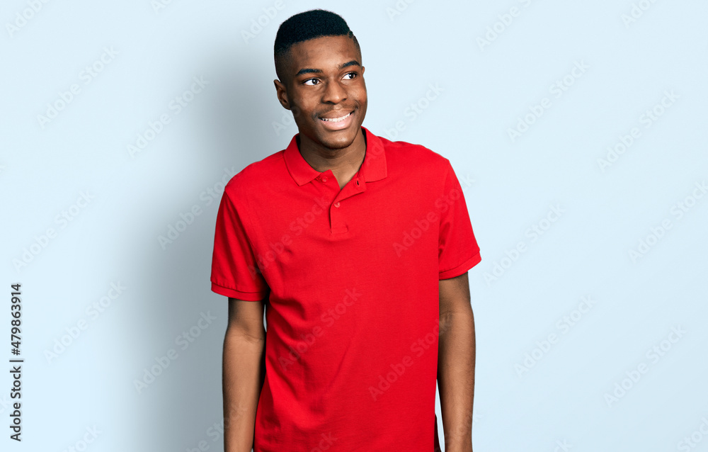 Young african american man wearing casual red t shirt looking away to side with smile on face, natural expression. laughing confident.