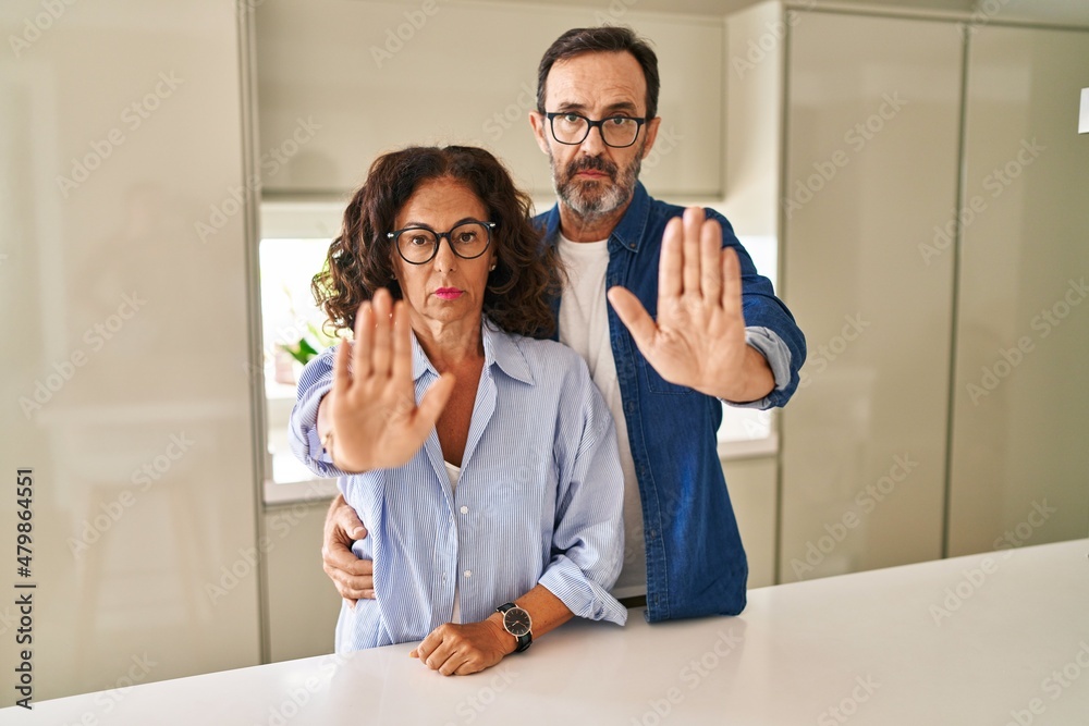 Middle age couple standing together doing stop sing with palm of the hand. warning expression with negative and serious gesture on the face. Middle age couple standing together doing stop sing with palm of the hand. warning expression with negative and serious gesture on the face.