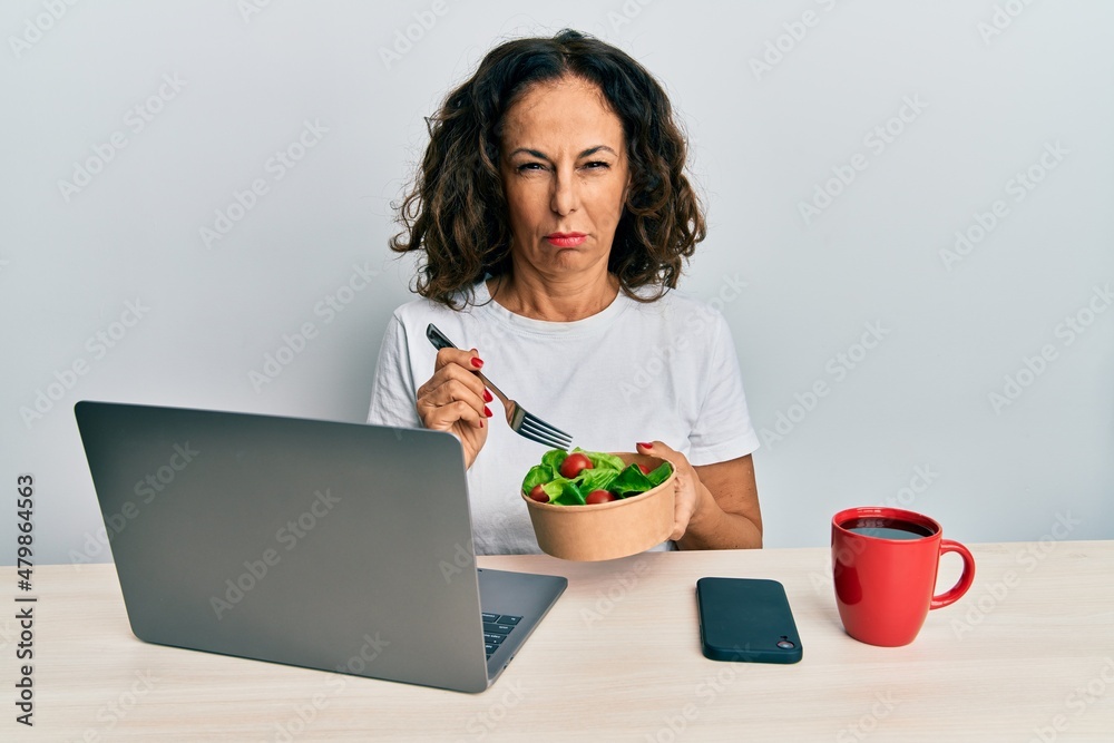 Beautiful middle age woman working at the office eating healthy salad skeptic and nervous, frowning upset because of problem. negative person. Beautiful middle age woman working at the office eating healthy salad skeptic and nervous, frowning upset because of problem. negative person.