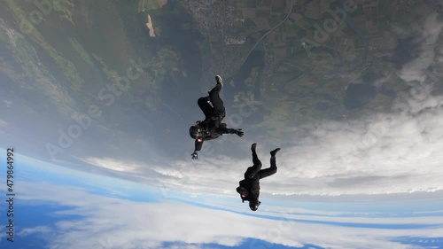 Sky divers free fall above green landscape
