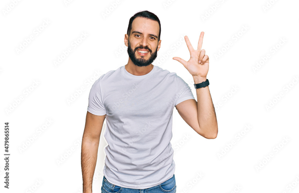 Young man with beard wearing casual white t shirt showing and pointing up with fingers number three while smiling confident and happy. Young man with beard wearing casual white t shirt showing and pointing up with fingers number three while smiling confident and happy.