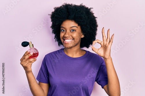 Young african american woman holding perfume doing ok sign with fingers, smiling friendly gesturing excellent symbol