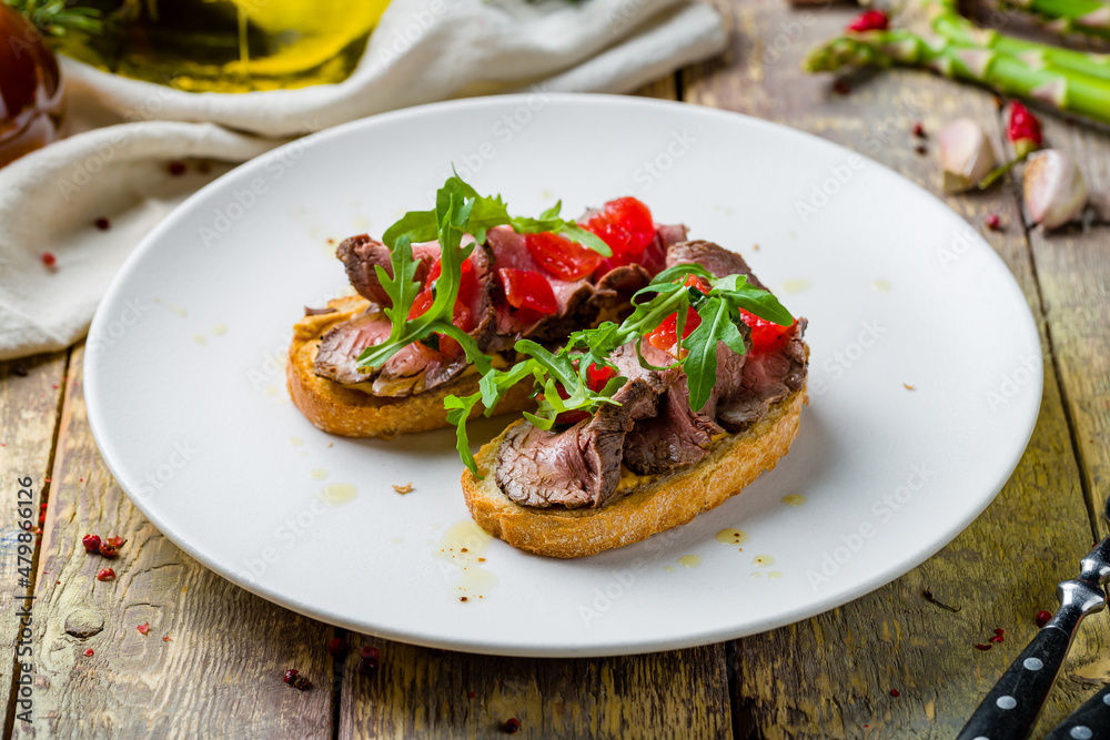 Bruschetta with roast beef on white plate on wooden table Bruschetta with roast beef on white plate on wooden table