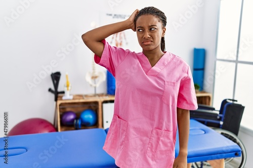Young african american woman working at pain recovery clinic confuse and wonder about question. uncertain with doubt  thinking with hand on head. pensive concept.
