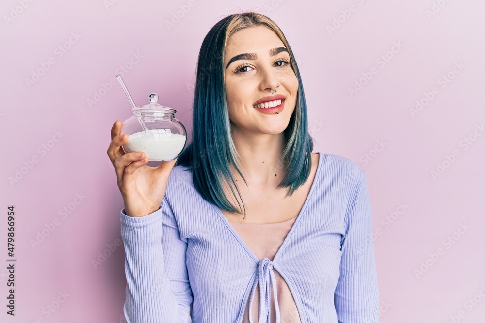 Young modern girl holding bowl with sugar looking positive and happy standing and smiling with a confident smile showing teeth Young modern girl holding bowl with sugar looking positive and happy standing and smiling with a confident smile showing teeth