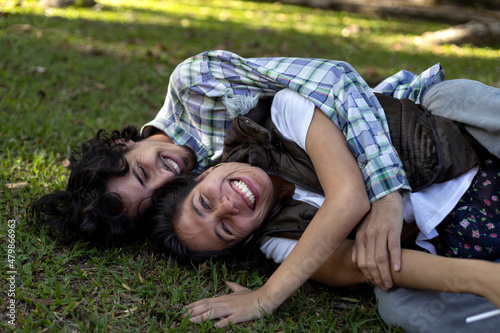 Young latin couple (28) lying on the grass, happily sharing Valentine's Day. Valentine's Day concept, couples and friendships.