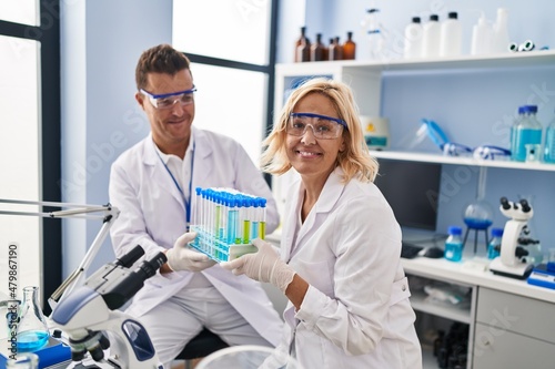 Middle age man and woman scientist partners holding test tube working at laboratory