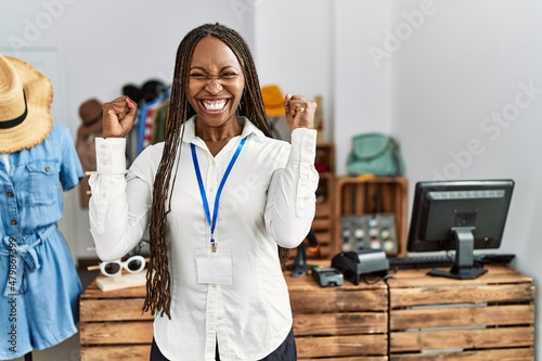 Black woman with braids working as manager at retail boutique excited for success with arms raised and eyes closed celebrating victory smiling. winner concept.