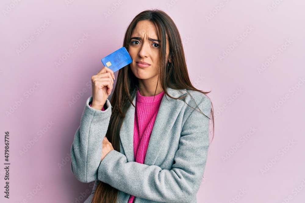 Young hispanic girl holding credit card clueless and confused expression. doubt concept. Young hispanic girl holding credit card clueless and confused expression. doubt concept.