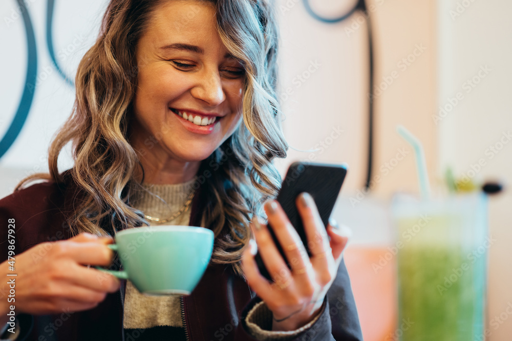 Beautiful young woman drinking coffee and using smartphone in a cafe Beautiful young woman drinking coffee and using smartphone in a cafe