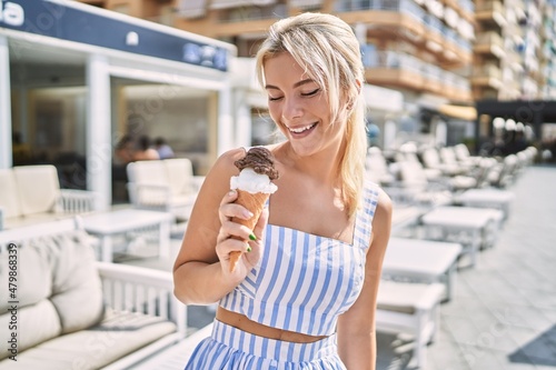 Young blonde girl smiling happy eating ice cream at the city.