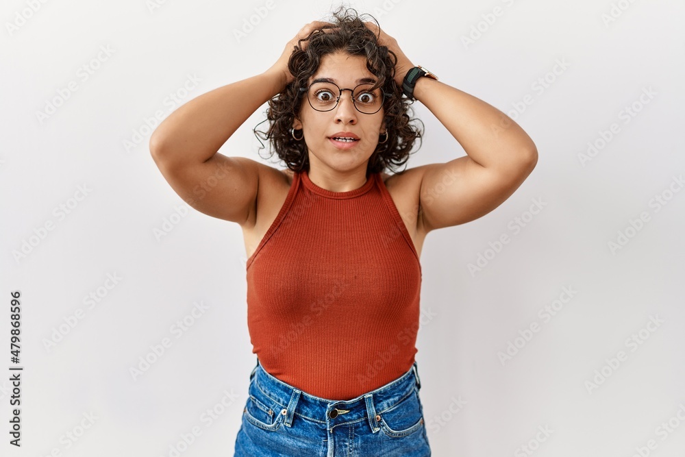 Young hispanic woman wearing glasses standing over isolated background crazy and scared with hands on head, afraid and surprised of shock with open mouth Young hispanic woman wearing glasses standing over isolated background crazy and scared with hands on head, afraid and surprised of shock with open mouth
