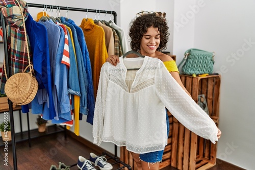 Young latin customer woman smiling happy holding hanger with clothes at clothing store