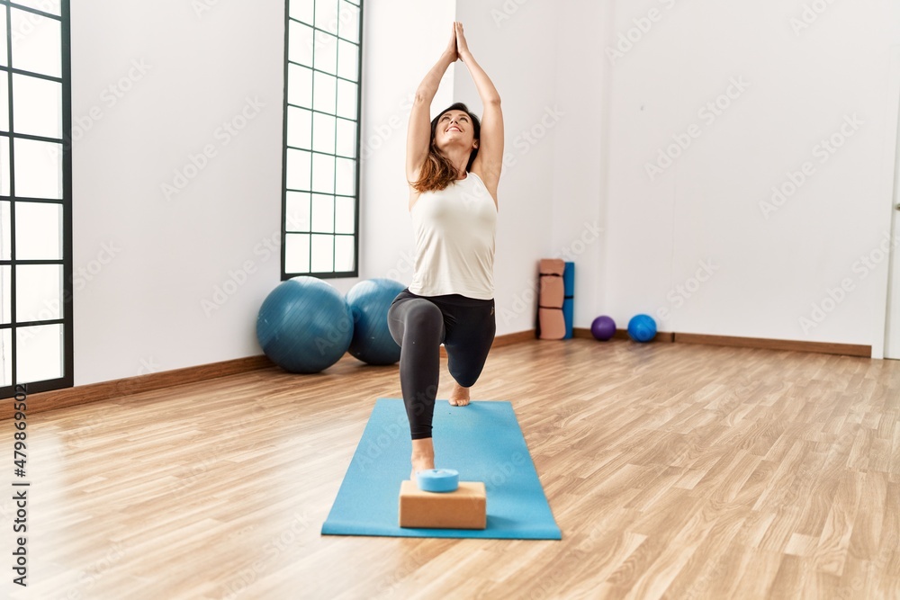 Middle age hispanic woman smiling confident training yoga at sport center