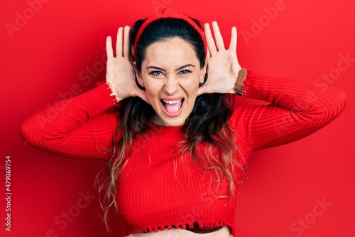 Young hispanic woman wearing casual clothes trying to hear both hands on ear gesture, curious for gossip. hearing problem, deaf