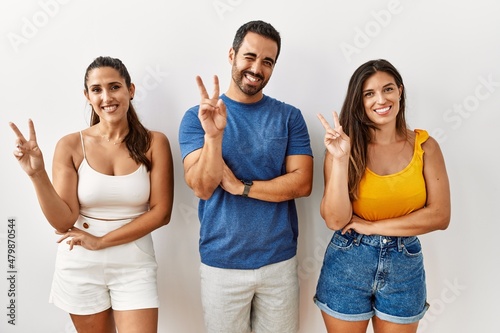 Group of young hispanic people standing over isolated background smiling with happy face winking at the camera doing victory sign with fingers. number two.