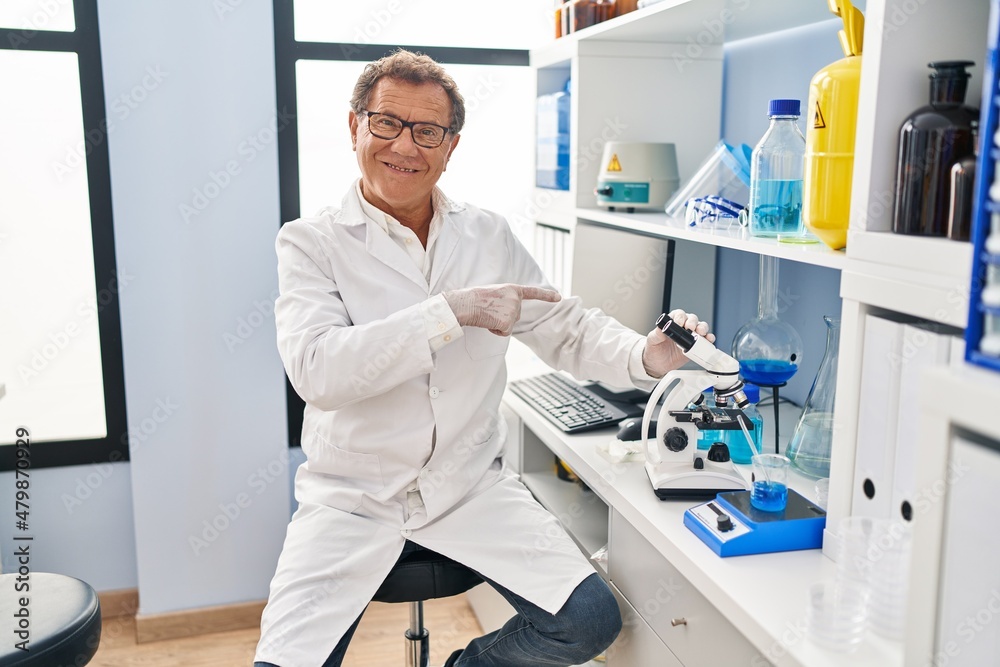 Senior man working at scientist laboratory smiling happy pointing with hand and finger Senior man working at scientist laboratory smiling happy pointing with hand and finger