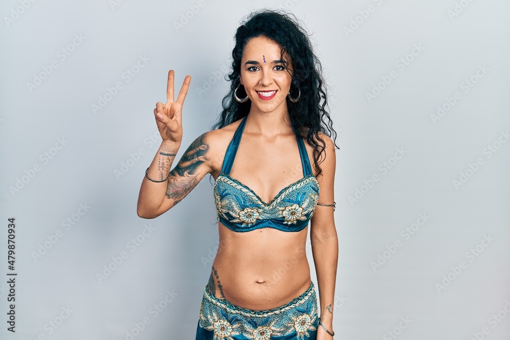 Fototapeta premium Young woman wearing bindi and traditional belly dance clothes showing and pointing up with fingers number two while smiling confident and happy.