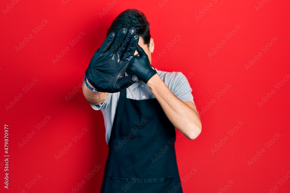 Young hispanic man wearing apron covering eyes with hands and doing stop gesture with sad and fear expression. embarrassed and negative concept. Young hispanic man wearing apron covering eyes with hands and doing stop gesture with sad and fear expression. embarrassed and negative concept.