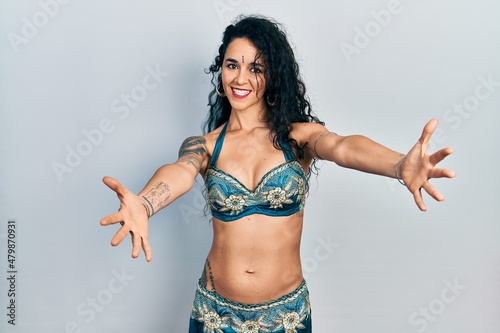 Young woman wearing bindi and traditional belly dance clothes looking at the camera smiling with open arms for hug. cheerful expression embracing happiness.