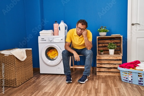 Middle age man sitting on chair waiting for washing machine at laundry room