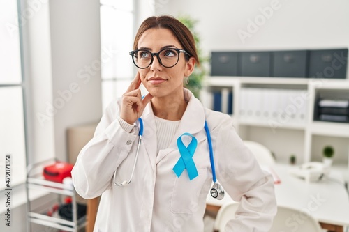 Young brunette doctor woman wearing stethoscope at the clinic with hand on chin thinking about question, pensive expression. smiling with thoughtful face. doubt concept.