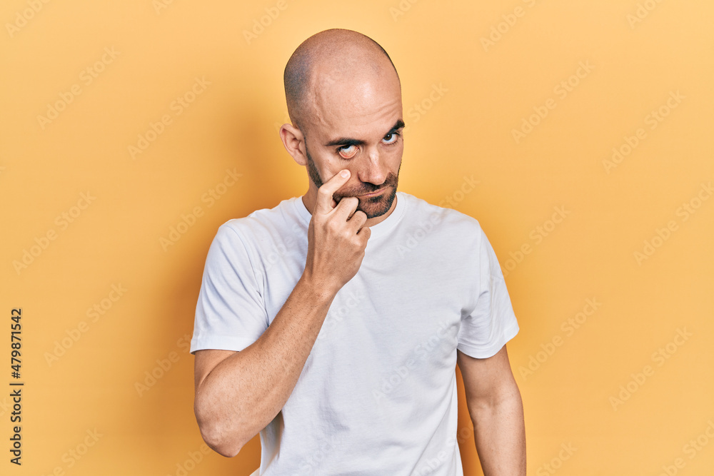 Young bald man wearing casual white t shirt pointing to the eye watching you gesture, suspicious expression Young bald man wearing casual white t shirt pointing to the eye watching you gesture, suspicious expression