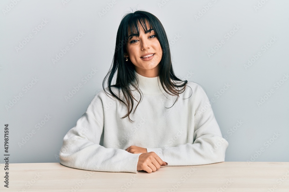 Young brunette woman with bangs wearing casual clothes sitting on the table with a happy and cool smile on face. lucky person. Young brunette woman with bangs wearing casual clothes sitting on the table with a happy and cool smile on face. lucky person.