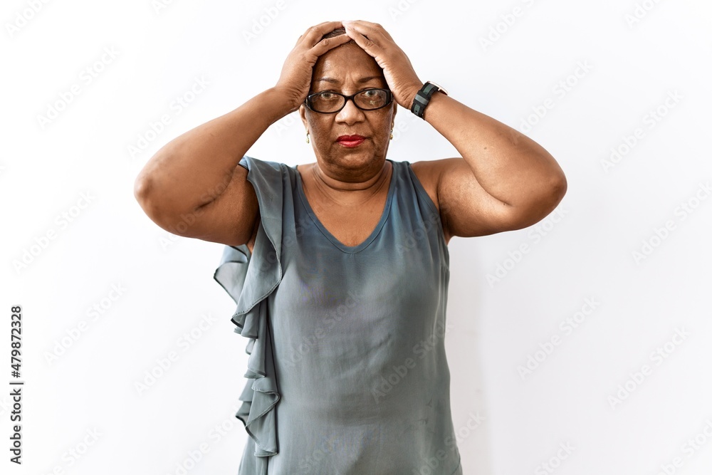 Fototapeta premium Mature hispanic woman wearing glasses standing over isolated background suffering from headache desperate and stressed because pain and migraine. hands on head.