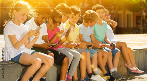 Group of positive kids sitting at urban street with mobile devices