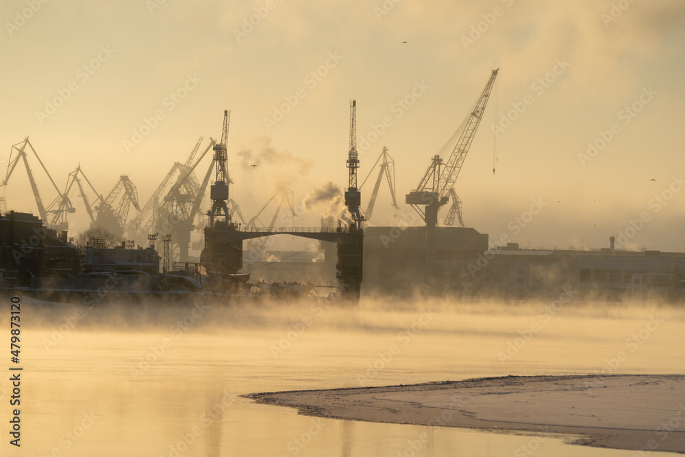 Cranes of Baltic shipyard in St. Petersburg in frosty winter day, steam over the Neva river, smooth surface of the river at sunset. 