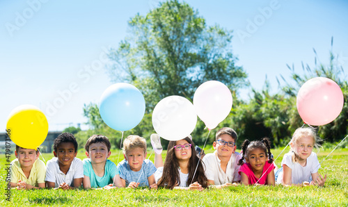 Happy kids with balloons lie on the green lawn. High quality photo © JackF