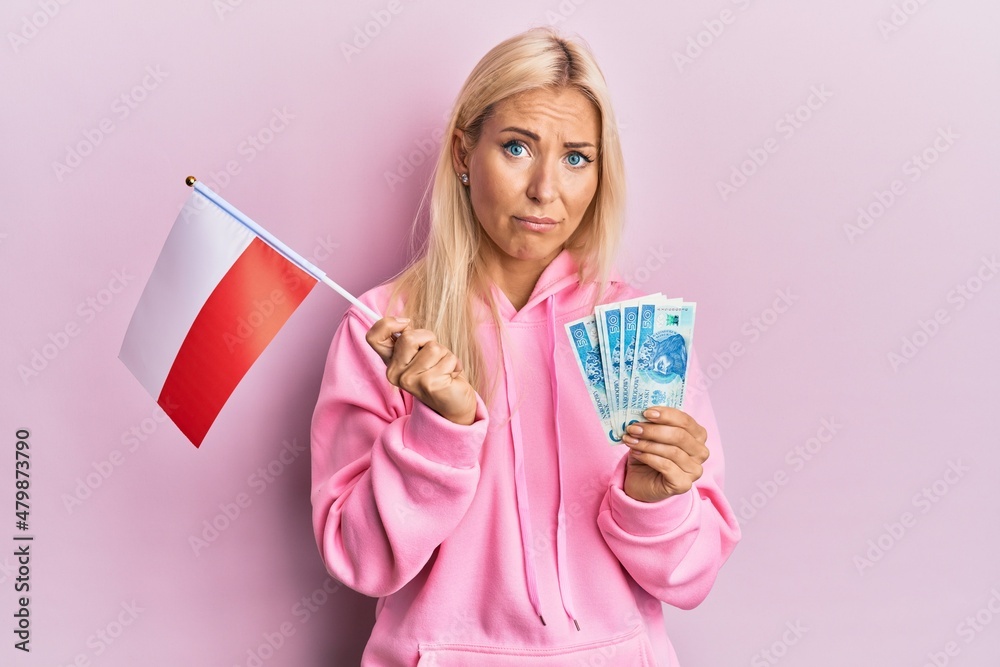 Young blonde woman holding poland flag and zloty banknotes skeptic and nervous, frowning upset because of problem. negative person. Young blonde woman holding poland flag and zloty banknotes skeptic and nervous, frowning upset because of problem. negative person.