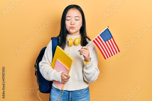 Young chinese girl exchange student holding america flag looking at the camera blowing a kiss being lovely and sexy. love expression.