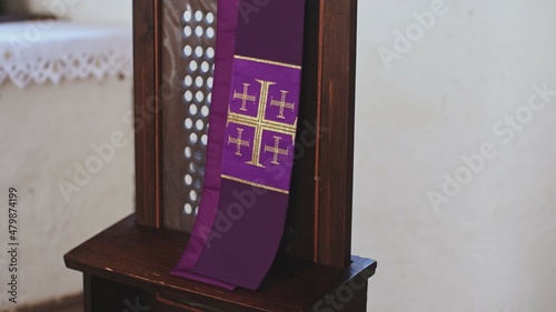 Purple Catholic Priest Stole with Embroidered Jerusalem Cross Hanging Over Grate of Simple Church Confessional	 photo