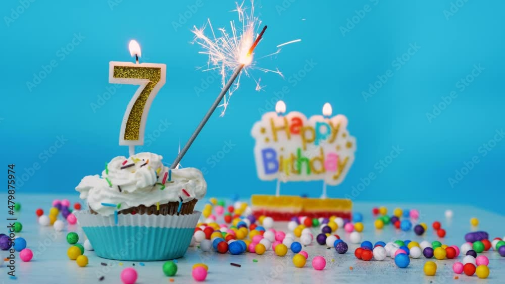 Beautiful Happy birthday greetings for a 7 year old child, birthday cupcake with candles and birthday decorations on a blue background. Copy space