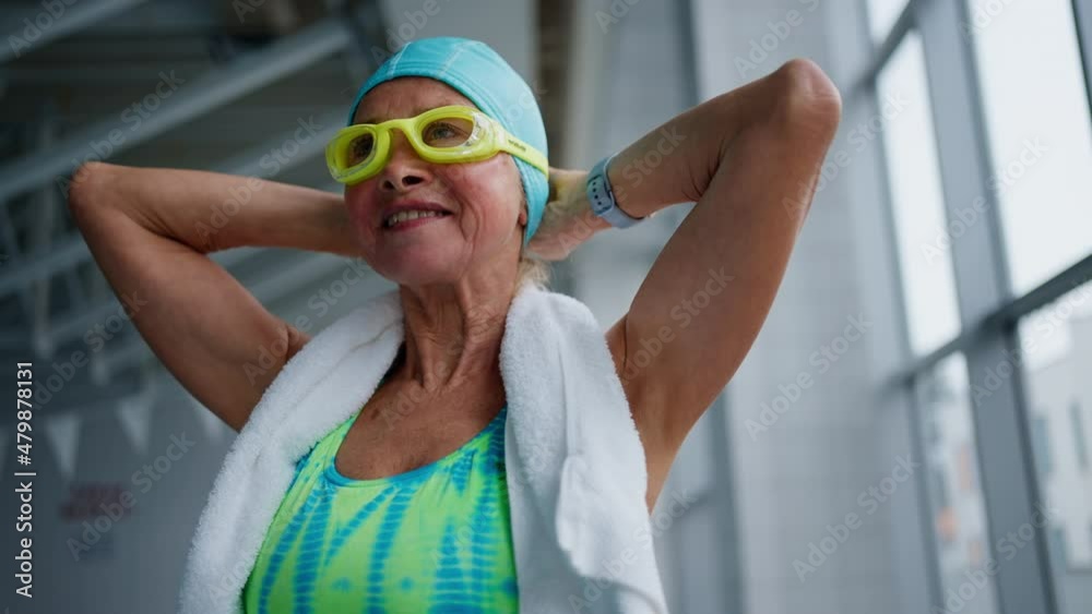Low angle view of senior woman putting on goggles before swim in indoors swimming pool.