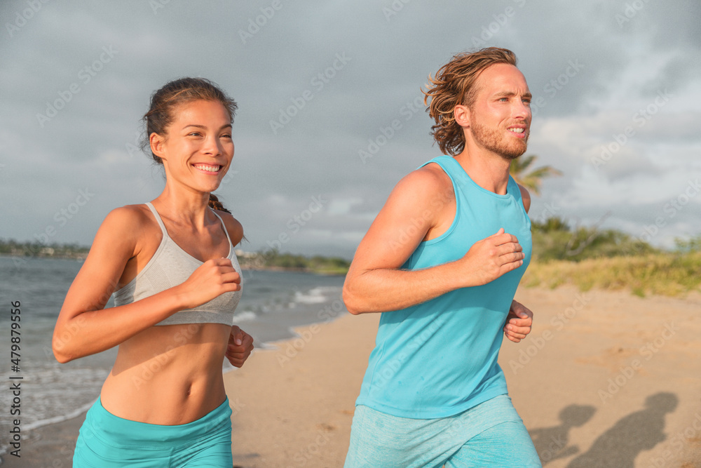 Portrait of happy running competitive couple smiling training together on summer beach. Asian fitness model, Caucasian male runner. Sports active lifestyle outdoor Portrait of happy running competitive couple smiling training together on summer beach. Asian fitness model, Caucasian male runner. Sports active lifestyle outdoor