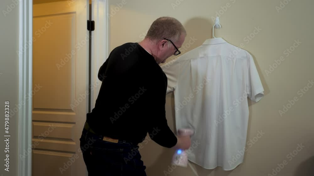Senior man using a steamer to remove wrinkles and disinfect a dress shirt for the first time Senior man using a steamer to remove wrinkles and disinfect a dress shirt for the first time