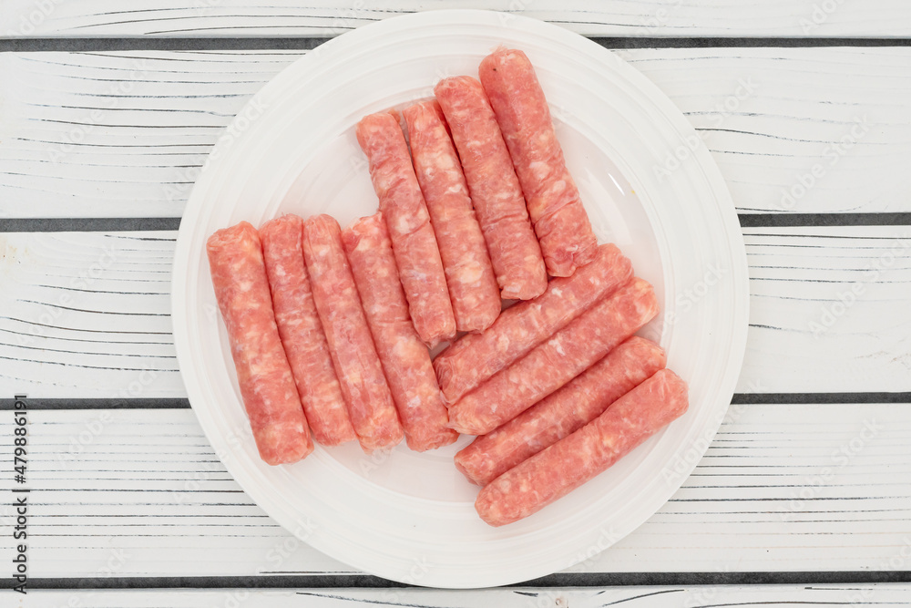 Raw chicken breakfast sausages close up on white plate on white wooden background, flat lay, copy space Raw chicken breakfast sausages close up on white plate on white wooden background, flat lay, copy space