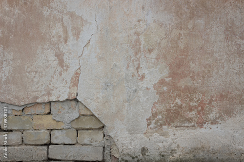 Old stone wall covered with cement. Half of cement on this wall is crumbled. There are bricks under the cement.	